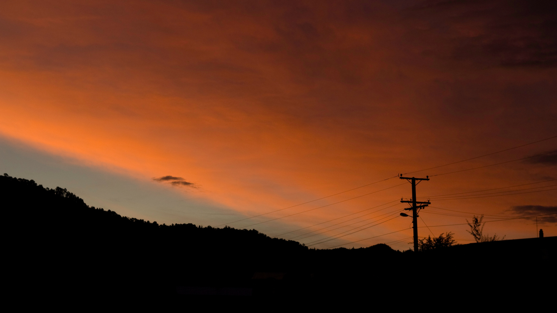 silhouette of power pole and power supply cables with sunset in the background. small stripe of clear sky on the left.