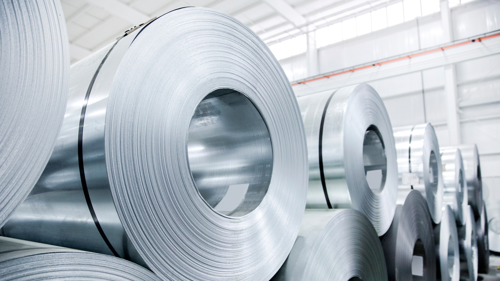 A photograph of multiple rolled aluminium metal sheets stored in a warehouse.